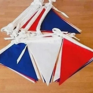 May include: A set of triangular bunting flags in red, white, and blue. The flags are attached to a white fabric cord with ties at the ends. The pennants are arranged in overlapping layers, showcasing a repeating pattern of solid primary colors.
