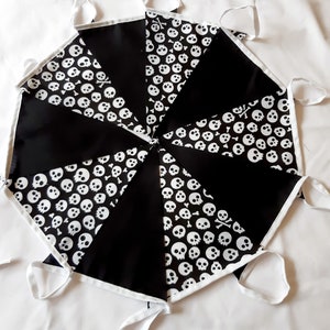 May include: A black and white skull and crossbones banner. The banner is made of triangular fabric pieces, alternating between solid black and a white skull pattern. White trim and ties complete the design.