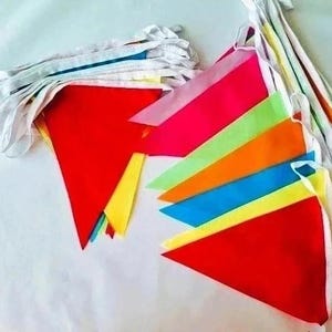 May include: A set of triangular bunting flags in vibrant colors including red, pink, lime green, orange, blue, and yellow, all attached to a white fabric ribbon. The pennants are arranged in overlapping stacks, showcasing a variety of bright hues.