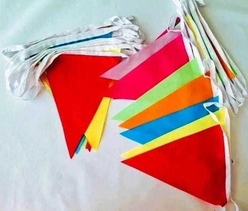 May include: A set of triangular bunting flags in vibrant colors including red, pink, lime green, orange, blue, and yellow, all attached to a white fabric ribbon. The pennants are arranged in overlapping stacks, showcasing a variety of bright hues.