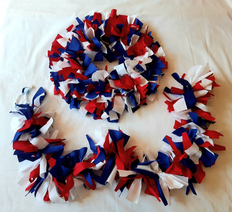 May include: A patriotic wreath and garland set. The wreath is circular, and the garland is long and flowing. Both are made of red, white, and blue fabric strips, perfect for Independence Day or other patriotic holidays.