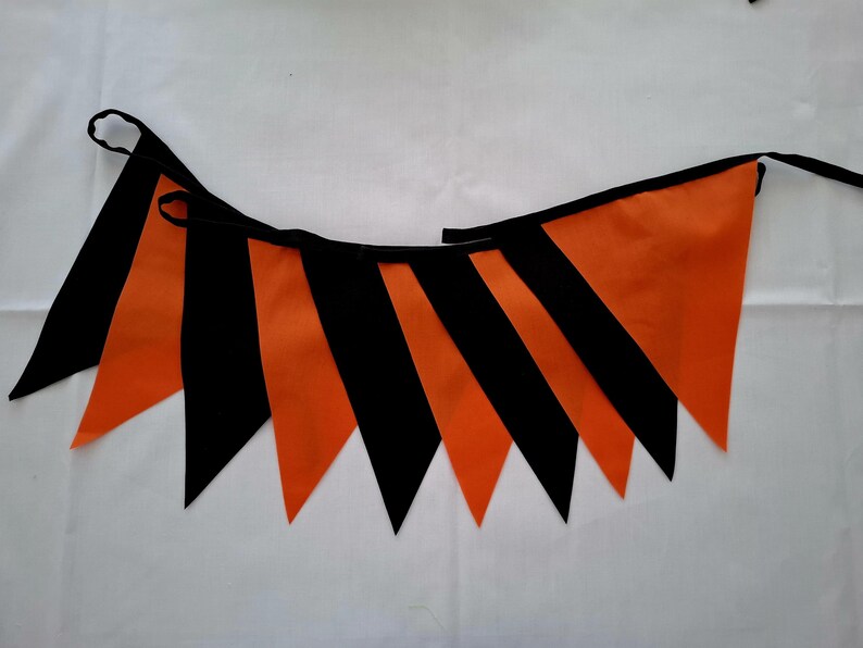 May include: A festive orange and black pennant banner. The triangular flags alternate between solid orange and black stripes, strung together with a black cord. Perfect for Halloween or other celebrations.