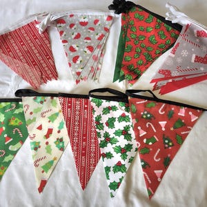 May include: A set of triangular fabric bunting flags featuring various Christmas-themed patterns including red and white Merry Christmas text, green holly leaves, candy canes, stockings, and Christmas trees, all attached to a black or white ribbon.