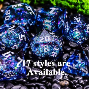 Pode incluir: Um conjunto de dados de resina azuis e transparentes com numeração prateada. Os dados são preenchidos com glitter e flocos iridescentes. O texto "17 styles are Available" é visível.