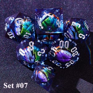 May include: A set of seven polyhedral dice with a galaxy-themed design. The dice are transparent with a blue hue, and feature silver numbering. The interior of each die has a colorful, swirling design. The text "Set #07" is at the bottom.