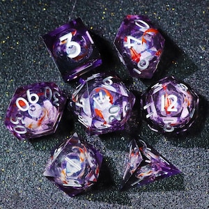 May include: Set of seven purple resin dice with white numbering. Each die features a miniature koi fish design with orange and white details. The dice are designed for tabletop gaming.