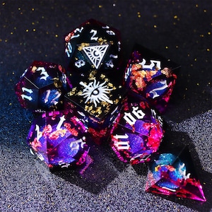 Pode incluir: Um conjunto de sete dados poliédricos em várias formas. Os dados são uma mistura de roxo, azul e vermelho com flocos dourados e numeração branca. Alguns dados apresentam símbolos brancos. Dados para jogos de tabuleiro.