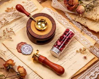Könnte beinhalten: Ein Wachssiegel-Set mit einem Schmelzlöffel mit Holzgriff, einem runden Schmelzofen aus Holz, einem Messingstempel mit Holzgriff und einem Glasfläschchen mit kleinen roten Wachsperlen. Zwei fertige Wachssiegel, eines rot und eines silber, liegen bei.