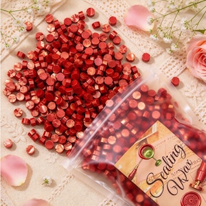 May include: A large collection of small, round, metallic red sealing wax beads. Some beads are loose, while others are contained within a clear plastic bag featuring a label with the text Sealing Wax and an illustration of a wax seal tool.