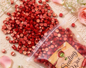 May include: A large collection of small, round, metallic red sealing wax beads. Some beads are loose, while others are contained within a clear plastic bag featuring a label with the text Sealing Wax and an illustration of a wax seal tool.