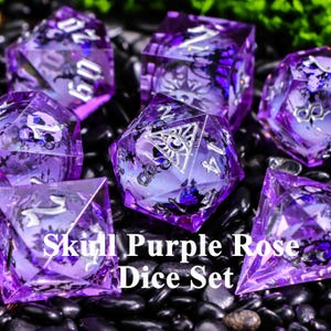 May include: A set of seven purple dice with silver numbering and skull and rose designs. The dice are made of a translucent material and are set against a black background. The text "Skull Purple Rose Dice Set" is visible.