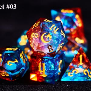 May include: Set #03. A set of polyhedral dice with a celestial theme. The dice are a mix of blue and red with gold numbering and symbols. The dice are made of a clear resin with a galaxy-like design.