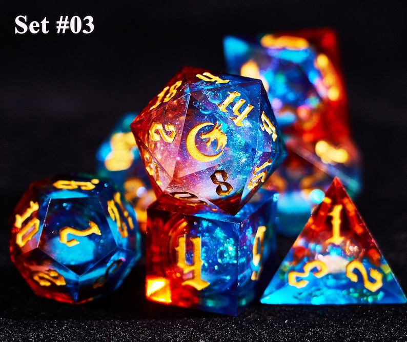 May include: Set #03. A set of polyhedral dice with a celestial theme. The dice are a mix of blue and red with gold numbering and symbols. The dice are made of a clear resin with a galaxy-like design.