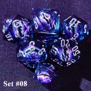 May include: A set of seven multi-sided dice with a galaxy-like design in shades of purple and blue. The dice have silver numbering and a detailed interior design. The text "Set #08" is visible.