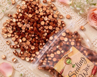 May include: A large collection of small, round, metallic copper-colored wax beads for sealing, with many loose beads scattered and others contained in a clear plastic bag featuring a label with the text Sealing Wax and a graphic illustration.