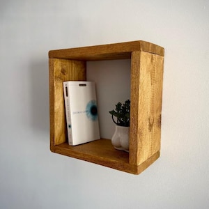 May include: A small, square, wooden shelf with a book titled "1984" by George Orwell and a small potted plant on it.