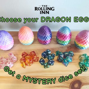 Op de afbeelding: De afbeelding toont vijf kleurrijke draken eieren en verschillende dobbelstenen sets. De eieren zijn in tinten paars, oranje, roze, blauw en groen. De dobbelstenen sets zijn in de kleuren transparant, oranje, blauw en groen. Tekst luidt "Choose your DRAGON EGG!" en "Get a MYSTERY dice set!"