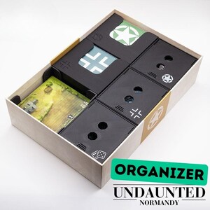 Può includere: Un organizer per scatola in legno per il gioco da tavolo Undaunted: Normandy. La scatola contiene scomparti neri con simboli militari e carte di gioco. La scatola ha il testo "ORGANIZER UNDAUNTED NORMANDY" in un banner verde e nero.