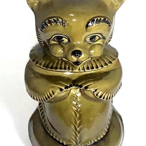 May include: A ceramic cookie jar shaped like a bear wearing a brown sweater. The bear has a brown face with black eyes and a black nose.