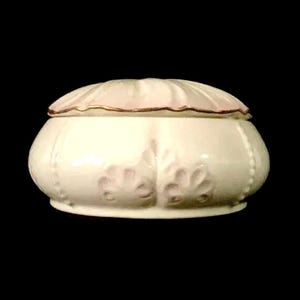 Peut inclure: Une boîte à bijoux en céramique blanche avec un couvercle rose et une bordure dorée. La boîte est ornée d'un motif floral et décorée de petites perles.