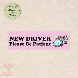 May include: A pink rectangular magnet or sticker with the text "NEW DRIVER Please Be Patient" in black. A cartoon cat is driving a light blue car. The magnet measures 10 inches by 3 inches.