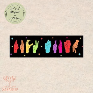 May include: A black rectangular magnet or sticker, 25.4 cm x 7.6 cm, displaying colorful hand gestures spelling a word. The hands are in various colours, including red, yellow, green, blue, and purple, with star accents.