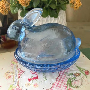 May include: A white ceramic mug with a black handle and the text "But First, Coffee" in a handwritten style. The mug is on a white surface. The mug is approximately 4 inches tall.