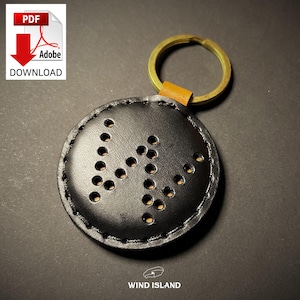 May include: Black leather keychain with a circle-shaped charm featuring a perforated design in the shape of the letter "M". The charm is attached to a gold-colored key ring.