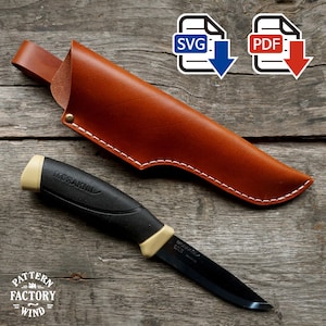 Puede incluir: Un cuchillo negro con mango beige y funda de cuero marrón. El cuchillo está etiquetado como "MORAKNIV". La funda está cosida con hilo blanco. La imagen también incluye iconos SVG y PDF.