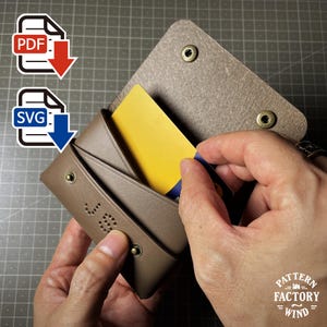 Puede incluir: Una cartera de cuero marrón con cierre de botón a presión, que contiene una tarjeta amarilla. La cartera tiene las iniciales "J.B." perforadas en la parte delantera. Iconos de archivos PDF y SVG.