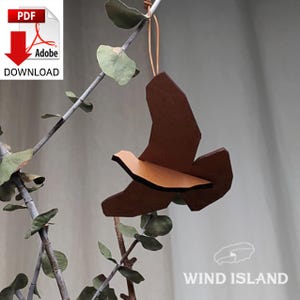 May include: A brown wooden bird ornament hanging from a branch. The bird is in flight with its wings spread out. The ornament is made of multiple pieces of wood that are joined together.