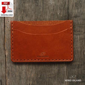 May include: A brown leather card holder with a stitched edge and the text "WIND ISLAND" embossed on the front.