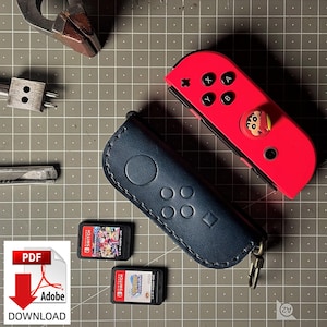 Puede incluir: Una funda de cuero azul oscuro con un diseño de mando de Nintendo Switch. La funda tiene una cremallera y un bucle para un llavero. También se muestran dos cartuchos de juego de Nintendo Switch.