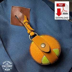 May include: A tennis ball keychain with a tan leather strap and a gold-colored ring. The keychain is attached to a blue backpack. The image also includes a PDF Adobe Download icon and the text "Pattern Factory Wind".