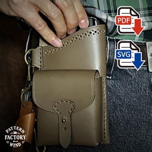 May include: A tan leather holster with a small pouch and a larger compartment, secured with a brass clasp. The holster is attached to a belt and features decorative stitching and a key ring. The text "PATTERN FACTORY WIND" is visible.