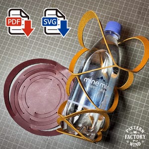 Puede incluir: Una botella de agua de plástico transparente con tapón azul dentro de un soporte de cuero color canela, junto a una pieza circular de cuero granate con orificios para costura. Iconos de descarga PDF y SVG visibles arriba a la izquierda.