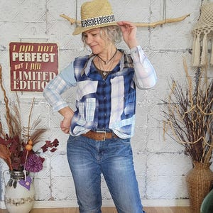 Könnte beinhalten: Eine Frau trägt ein Patchwork-Hemd mit blauem Karomuster, eine blaue Jeans und braune Stiefel. Sie trägt auch einen Strohhut mit gemustertem Band. Ein Schild im Hintergrund lautet: "I AM NOT PERFECT BUT I AM LIMITED EDITION."