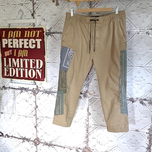 Peut inclure: Pantalon beige avec une taille à cordon et des détails de patchwork. Le patchwork est fait de tissus de différentes couleurs avec des motifs paisley et floraux.