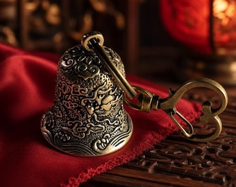 May include: A brass-toned metal bell keyring featuring intricate embossed patterns of clouds and waves. The bell is attached to a heart-shaped lobster clasp, showcasing a weathered, antique-style finish with dark recessed detailing.