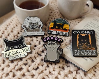 Broches de esmalte de gato e guaxinim: acessórios sarcásticos e bem-humorados