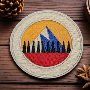 May include: Embroidered patch with a mountain and forest design. The patch features a beige border, a yellow sky, blue and white mountain peaks, and a red and black forest. A compass and pinecone are in the background.