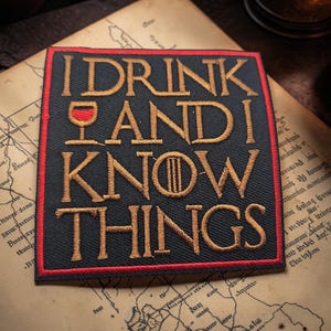 May include: A square black embroidered patch with a red border featuring the gold text I DRINK AND I KNOW THINGS. The letter O in KNOW is replaced by a circular symbol with three vertical lines, and a small red wine glass icon sits beside I.