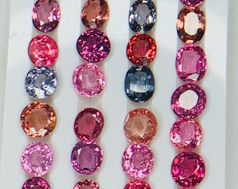May include: An assortment of oval and round gemstones in various shades of pink, purple, and gray. The gems are arranged in neat rows on a white surface, showcasing their polished facets and vibrant colors. The gemstones are likely for jewelry making.