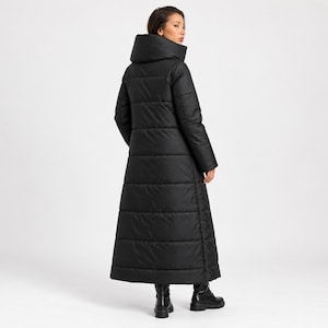 Peut inclure: Un long manteau matelassé noir doté d'un col haut structuré et de coutures horizontales. Le manteau descend jusqu'aux chevilles et est associé à des bottes en cuir noir, présentant une silhouette longue et épurée.