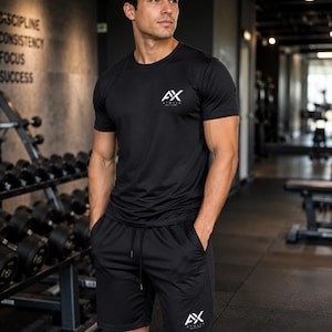 Pode incluir: Uma t-shirt preta de manga curta com gola redonda e calções desportivos pretos a combinar. A t-shirt apresenta um logótipo AX branco no peito esquerdo e os calções têm um logótipo AX branco na perna esquerda. Ambas as peças têm acabamento.