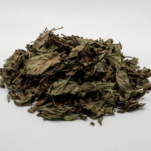 May include: A pile of dried green mint leaves on a white background.