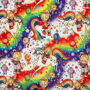 May include: A fabric print featuring a repeating pattern of cartoon characters with blonde hair, white horses with rainbow manes, and small colorful creatures. The background is a vibrant rainbow gradient filled with scattered stars.