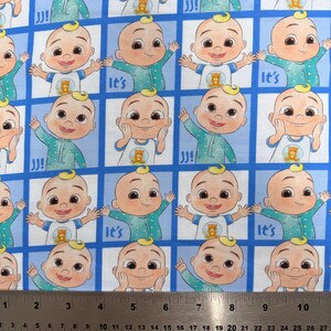 May include: A blue and white patterned fabric featuring a repeating grid of cartoon characters in green pajamas, with some squares displaying the text "It's". A metal ruler is positioned at the bottom, showing measurements up to 10.5 inches.