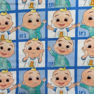 May include: A repeating fabric pattern featuring cartoon baby characters with light skin, small tufts of blonde hair, and teal pajamas. The characters are set within blue-bordered white squares, interspersed with the text It's and JJ in blue.