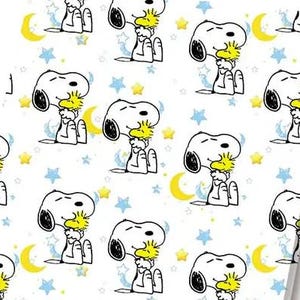 Op de afbeelding: Een wit stofpatroon met een herhalende illustratie van de witte hond Snoopy die de gele vogel Woodstock knuffelt. Het ontwerp bevat verspreide gele maansikkels, kleine gele sterren en lichtblauwe sterren over het oppervlak.